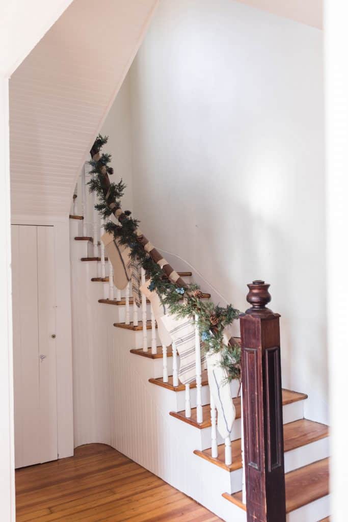 Antique farmhouse stairs wrapped in greenery and stocking hung for a farmhouse Christmas tour