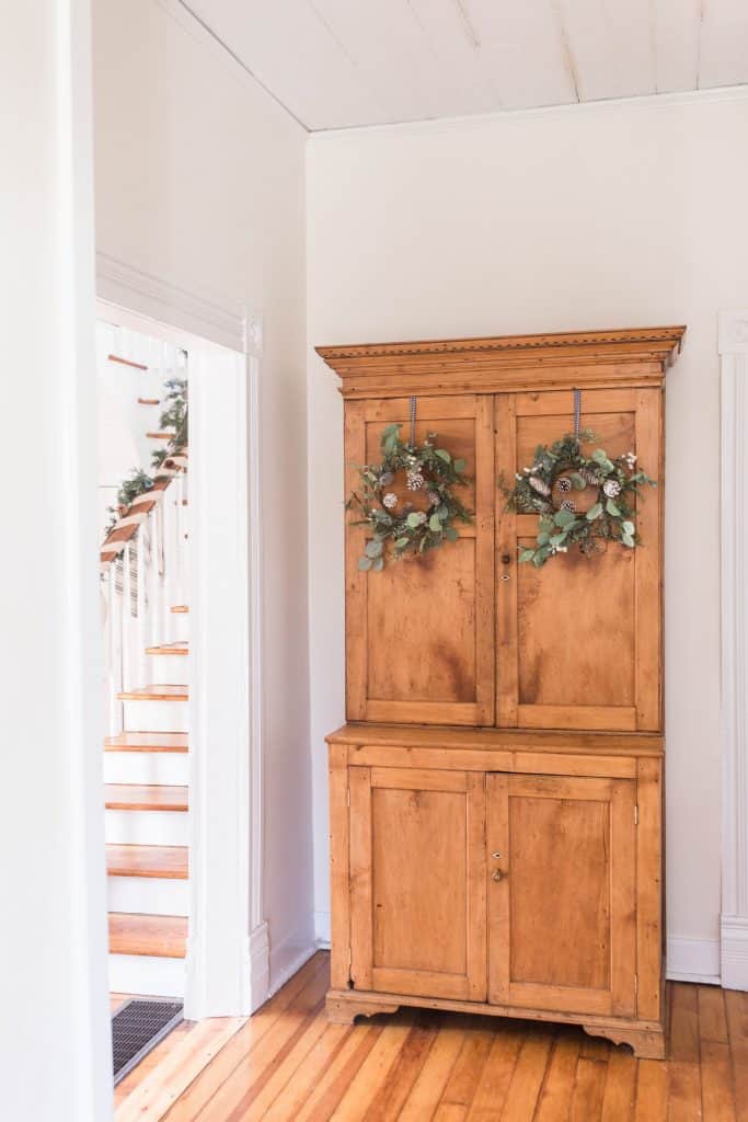 antique wood cabinet with two wreaths hung on the doors