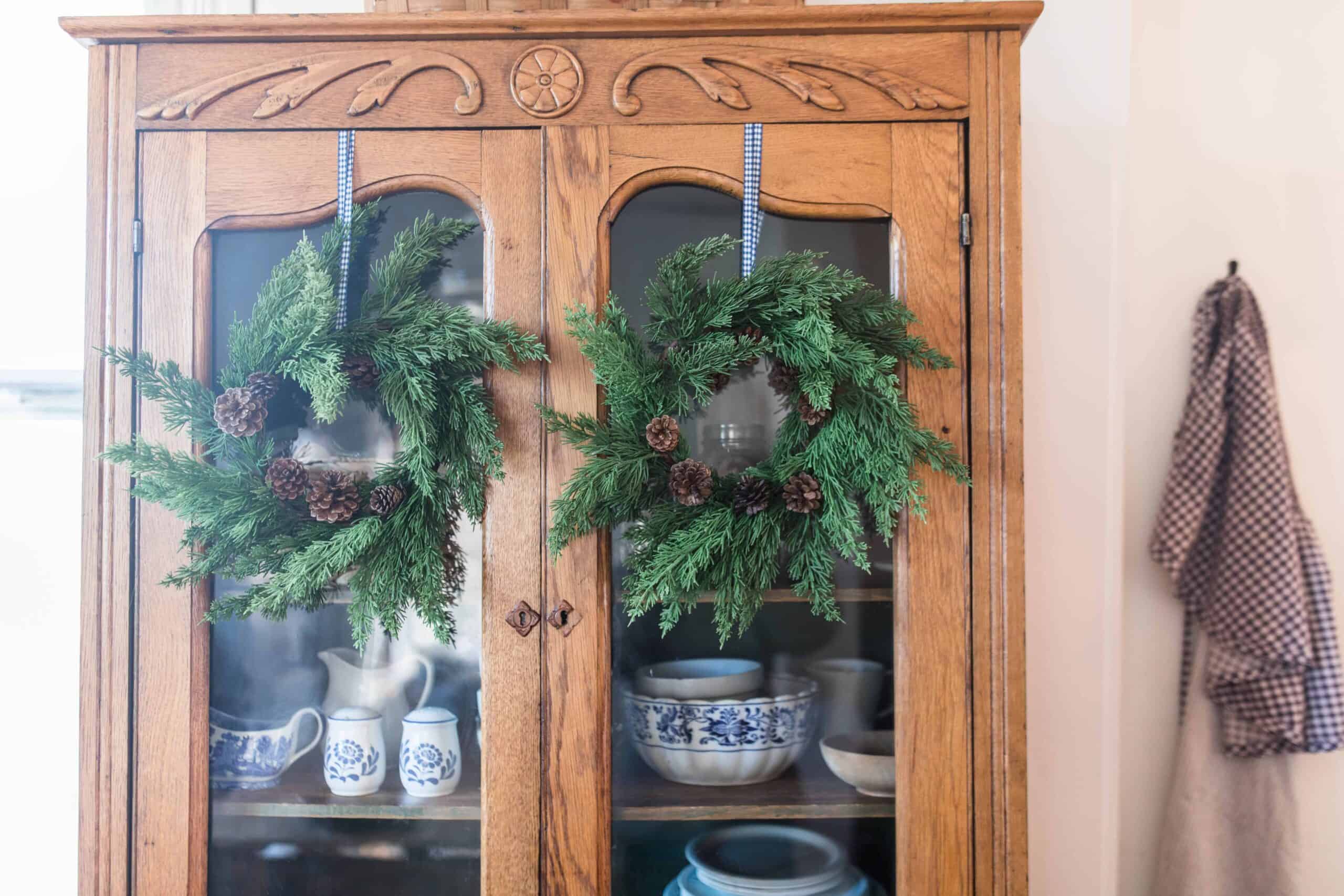 greenery wreaths hung with ribbon on an antique hutch for farmhouse Christmas tour