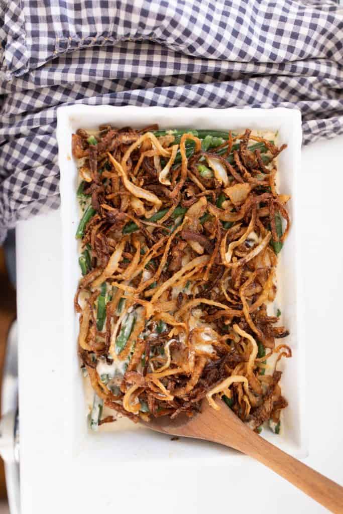 classic green bean casserole made from scratch with homemade fried onions on a white countertop next to a blue and white checked towel.