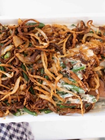 homemade classic green bean casserole from scratch topped with fried onions. A wooden spoon is in the dish.