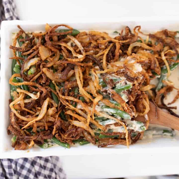 homemade classic green bean casserole from scratch topped with fried onions. A wooden spoon is in the dish.