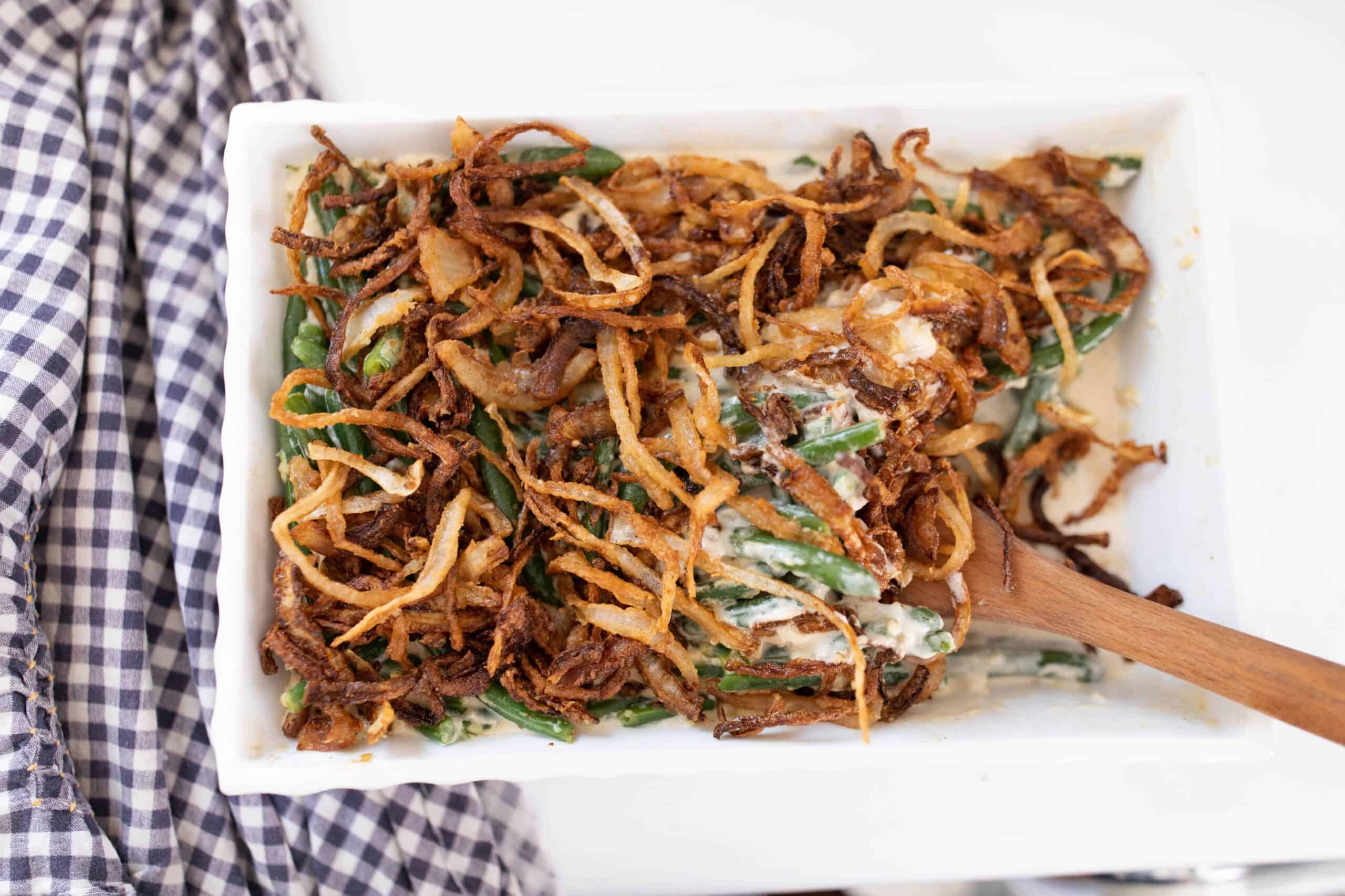 homemade classic green bean casserole from scratch topped with fried onions. A wooden spoon is in the dish.