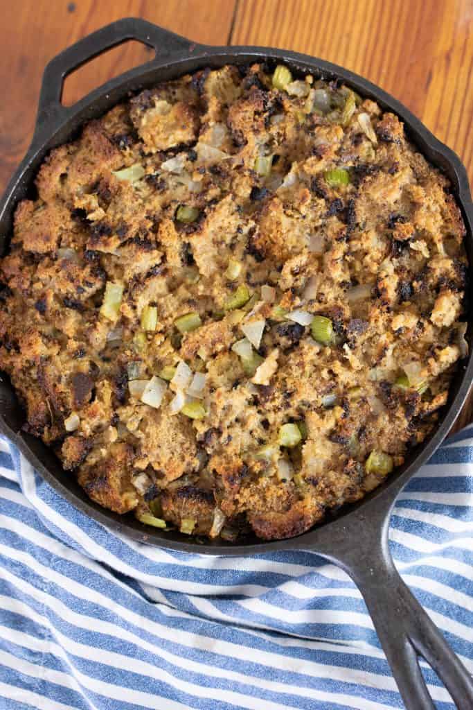 homemade sourdough stuffing from scratch in a cast iron skillet on top a blue and white stripped towel