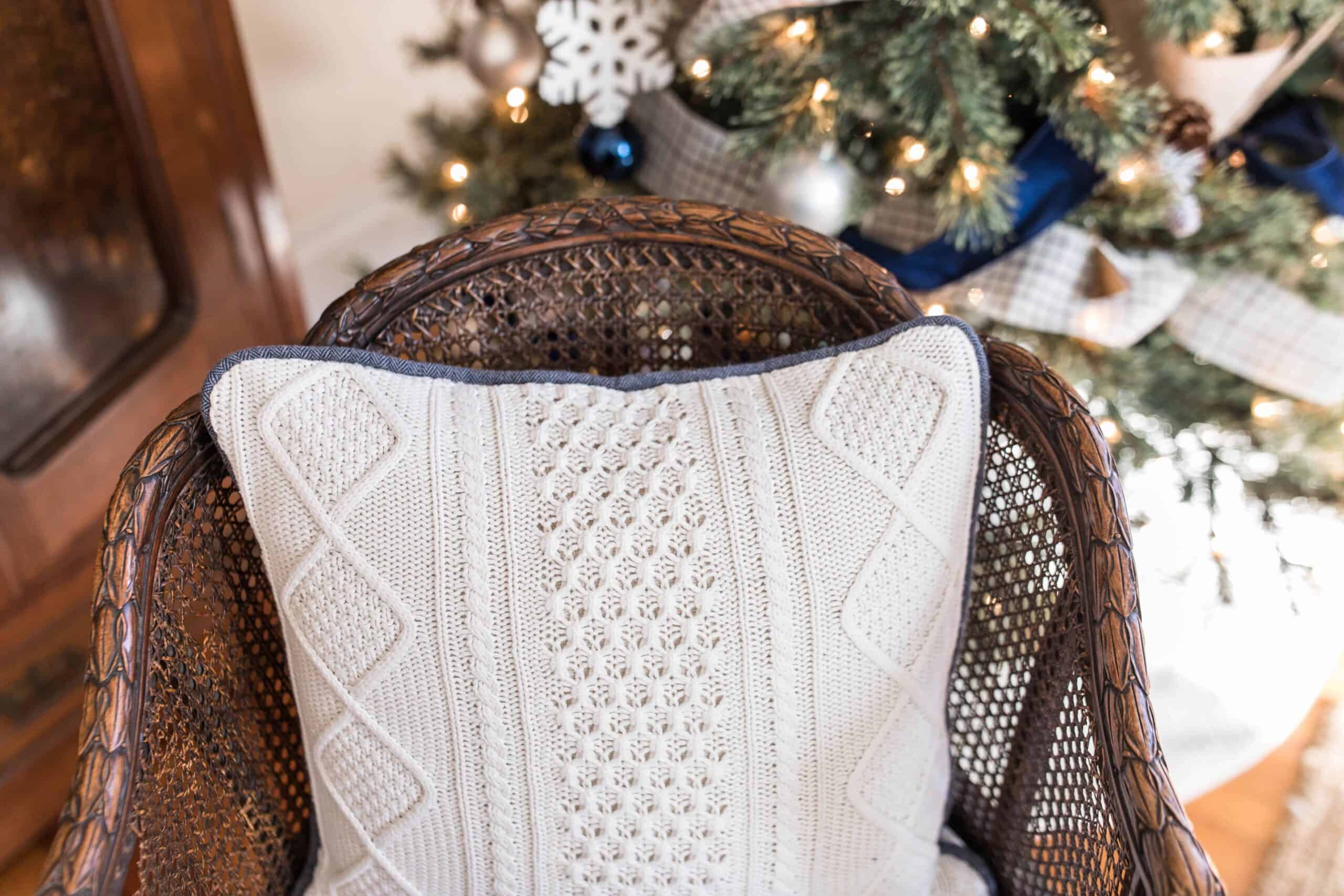 pillow made from a white sweater with blue piping on a wood chair with a Christmas tree in the background
