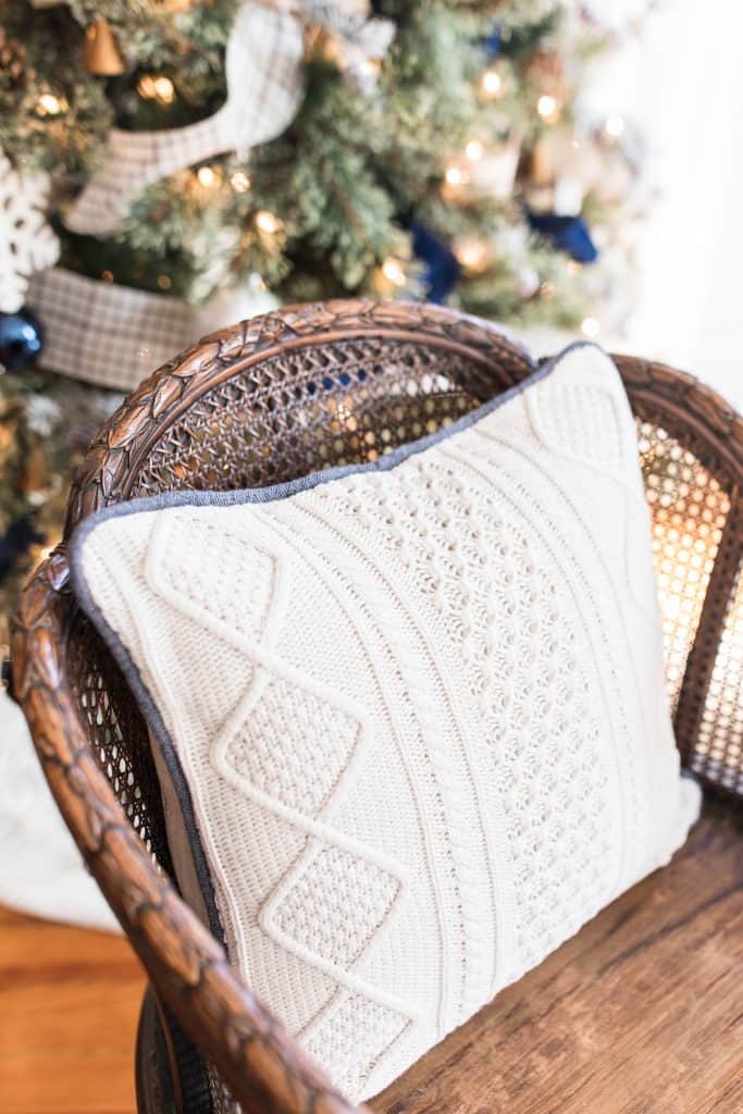 white sweater pillow on a wood chair with a Christmas Tree in the background