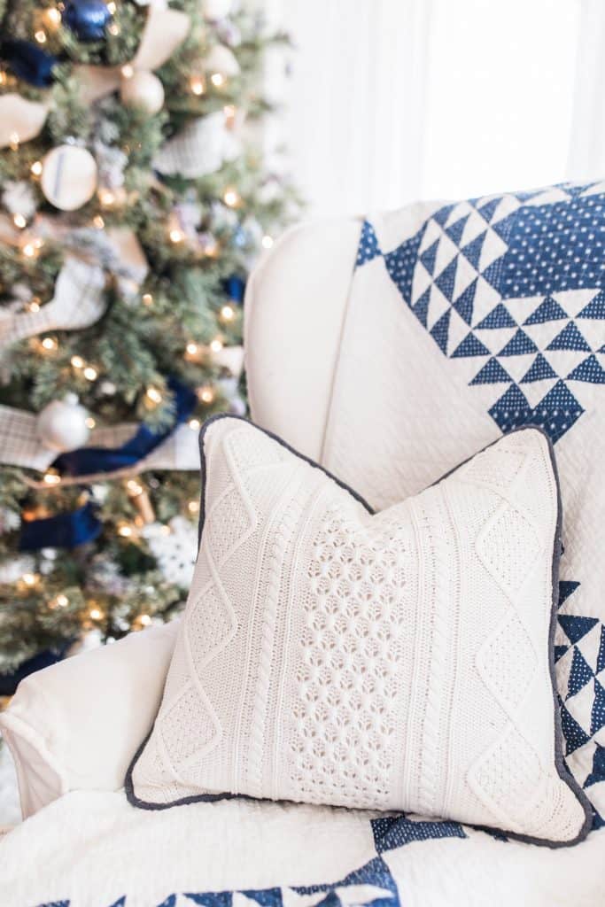 sweater pillow with blue cording on a white wing-back chair with a blue and white quilt draped over the back.