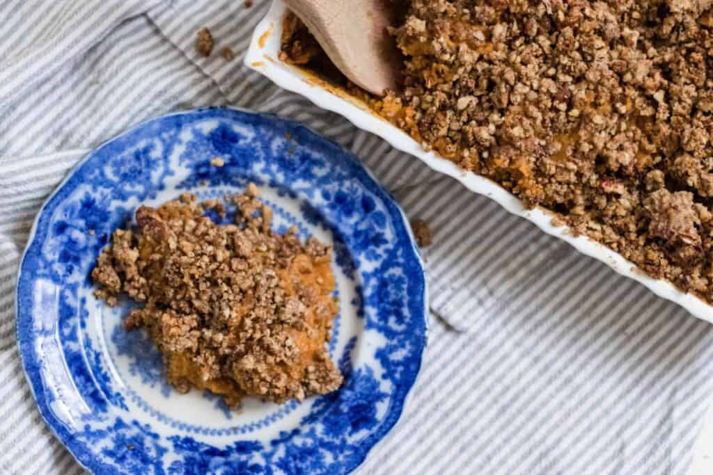 healthy sweet potato casserole recipe with pecan topping on a blue and white antique plate and a baking dish with the remaining sweet potato casserole in a baking dish behind