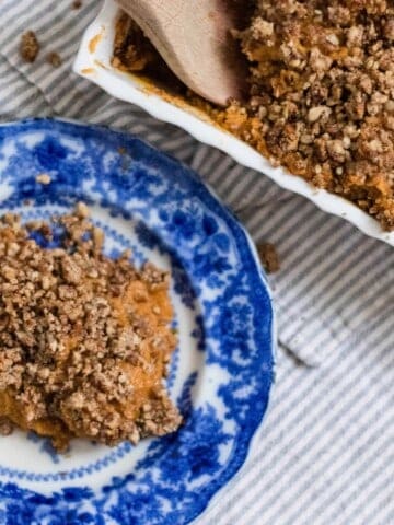 healthy sweet potato casserole recipe with pecan topping on a blue and white antique plate and a baking dish with the remaining sweet potato casserole in a baking dish behind