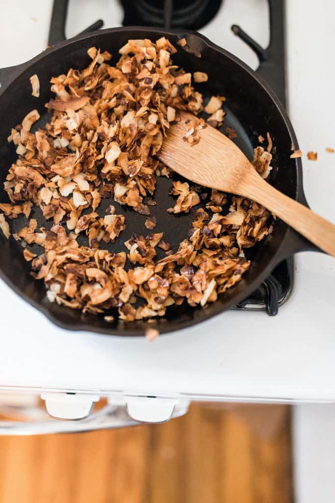 toasting shredded coconut in a cast iron skillet with a wooden utensil