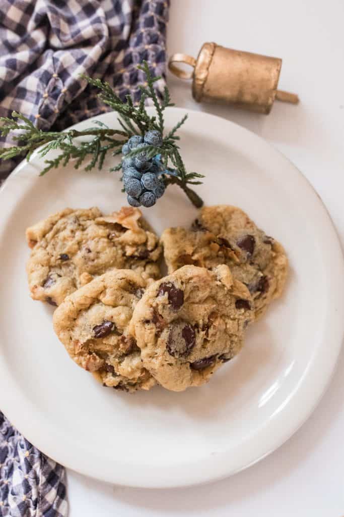 a white plate with einkorn chocolate chip cookies with a piece of greenery for decorations. The plate tests on a blue and white plaid towel and quartz countertop