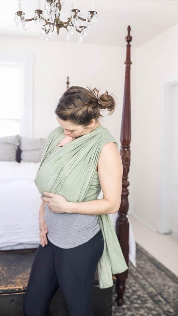 women wearing a baby in a wrap kissing baby's head 