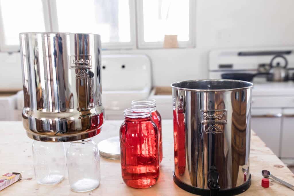 Berkey Water filter over two clean mason jars with two half gallon mason jars to the right with red dye and the bottom canister to the right - Berkey red dye test