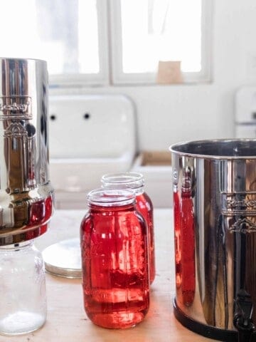 Berkey Water filter over two clean mason jars with two half gallon mason jars to the right with red dye and the bottom canister to the right - Berkey red dye test