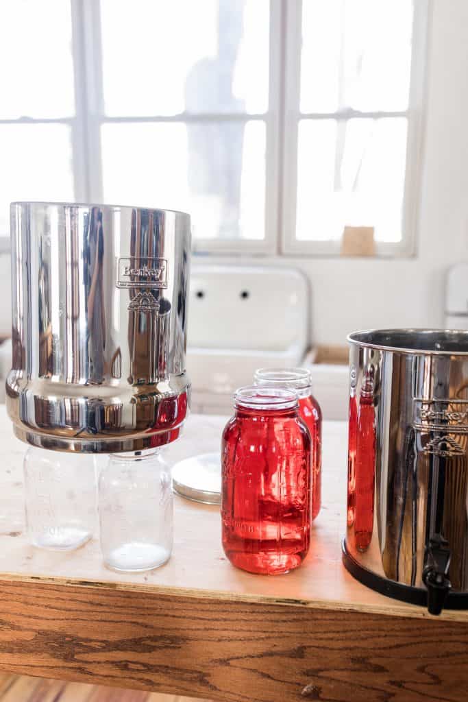 Berkey Water filter over two clean mason jars with two half gallon mason jars to the right with red dye.