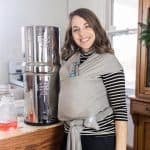 women wearing a baby standing next to a Berkey Water filter smiling.