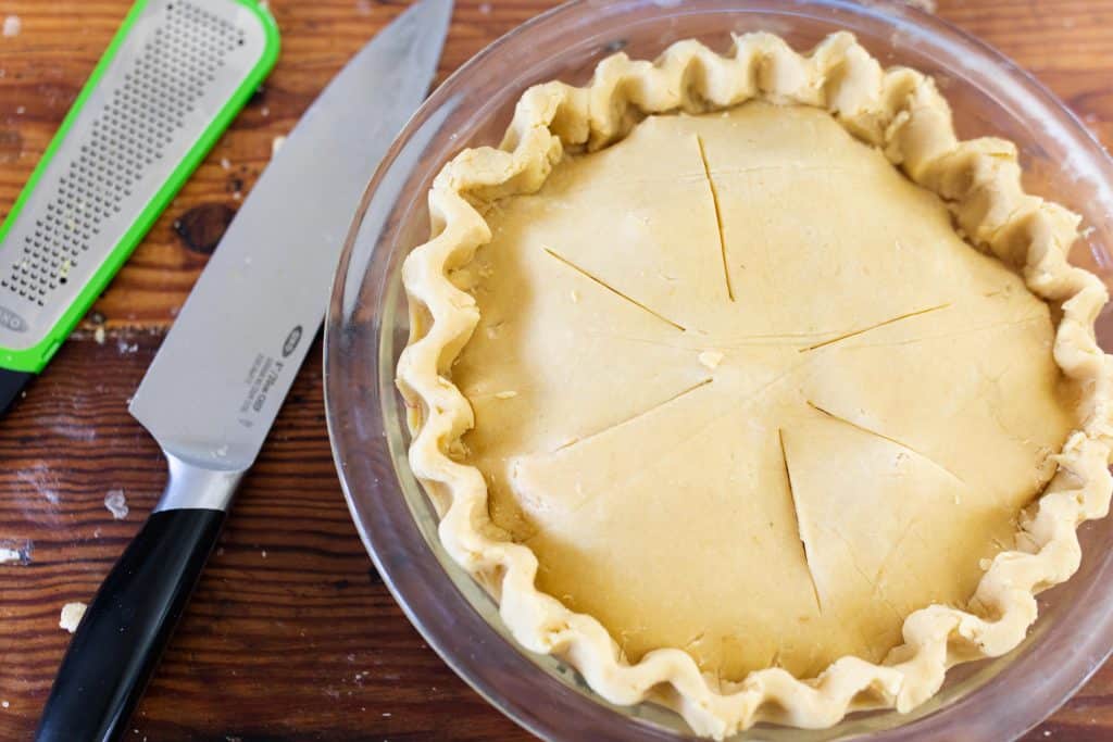 apple pie ready for the oven to be baked. A Knife and zester to the left of the pie