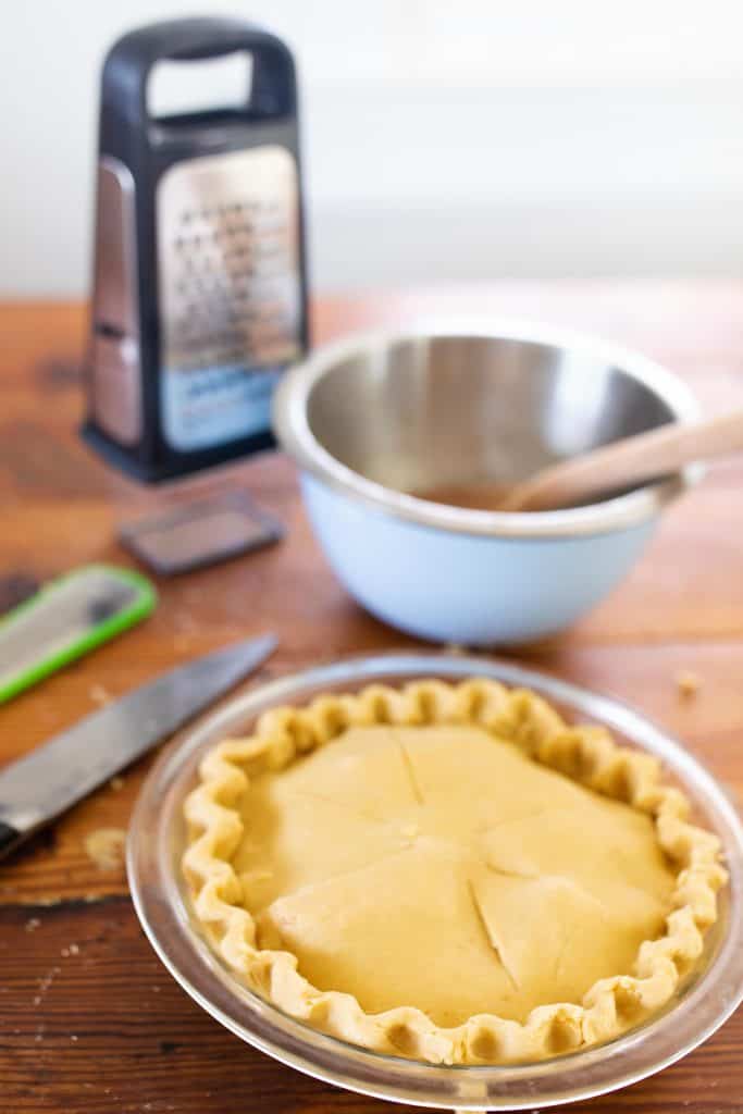 einkorn apple pie in a glass dish with bowl and cheese grater behind