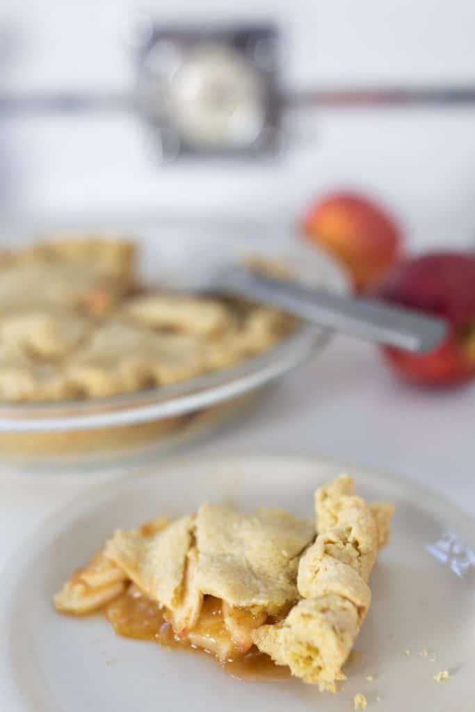 slice of homemade apple pie made with einkorn crust on a plate with the remaining pie in a glass pie dish behind