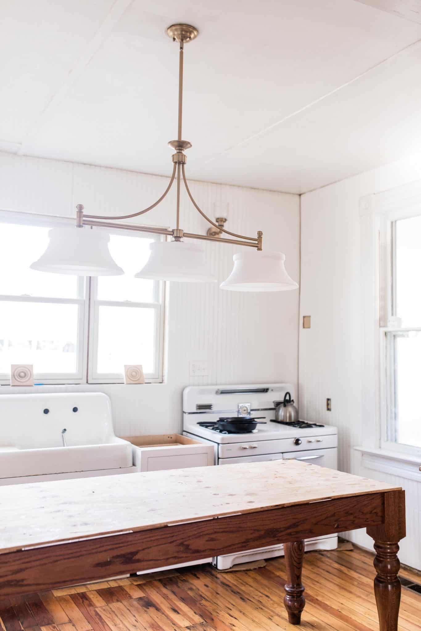 victorian farmhouse kitchen update with new white cabinets, antique sink and stove, and a handmade island. New brass lighting hands over the island