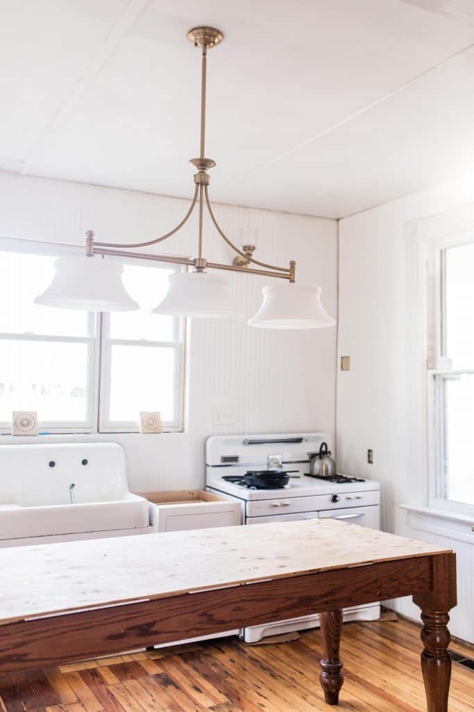 victorian farmhouse kitchen update with new white cabinets, antique sink and stove, and a handmade island. New brass lighting hands over the island 