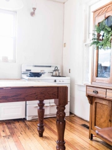 farmhouse kitchen during renovation with a table island, wooden hutch, and antique stove in the background