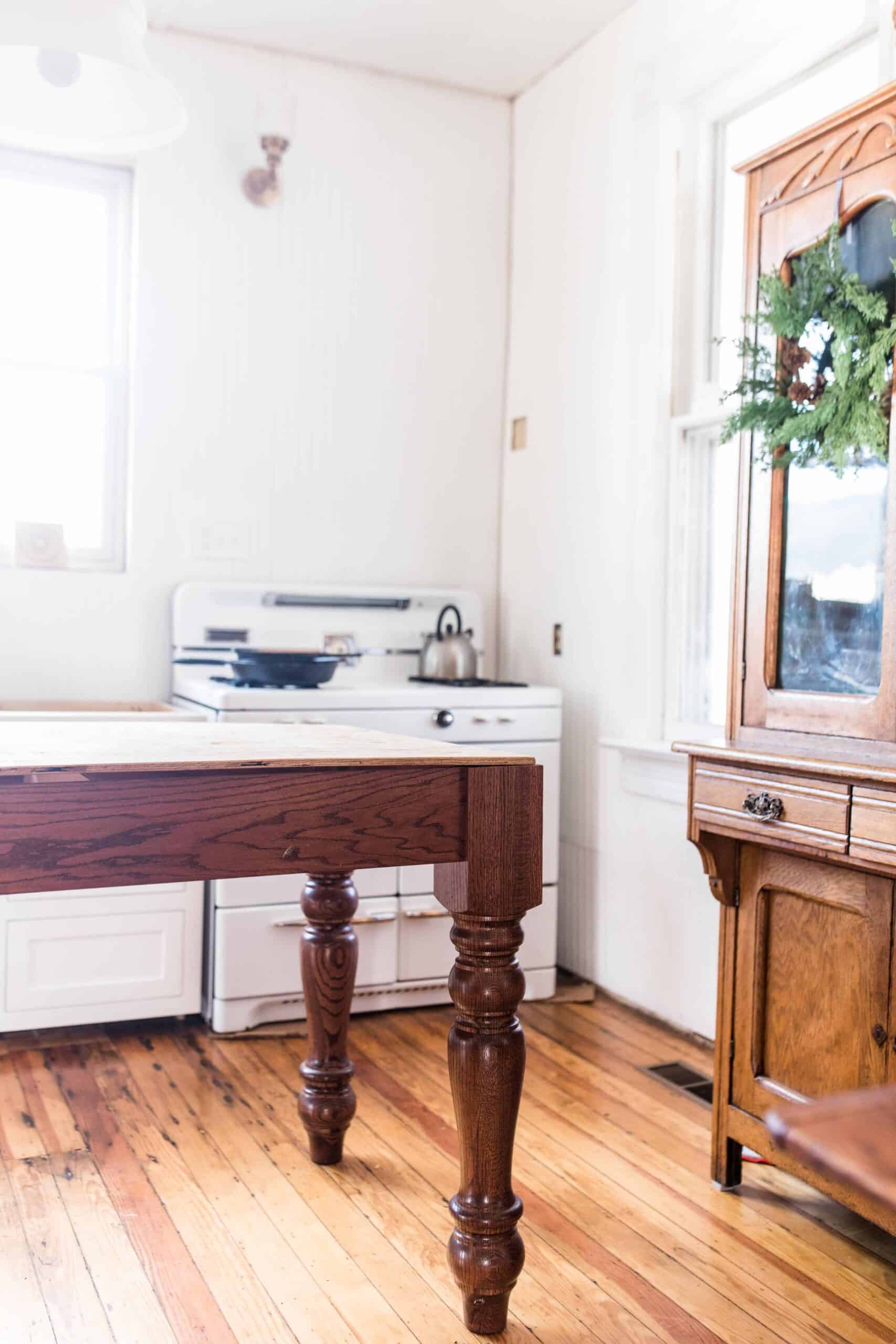 farmhouse kitchen during renovation with a table island, wooden hutch, and antique stove in the background