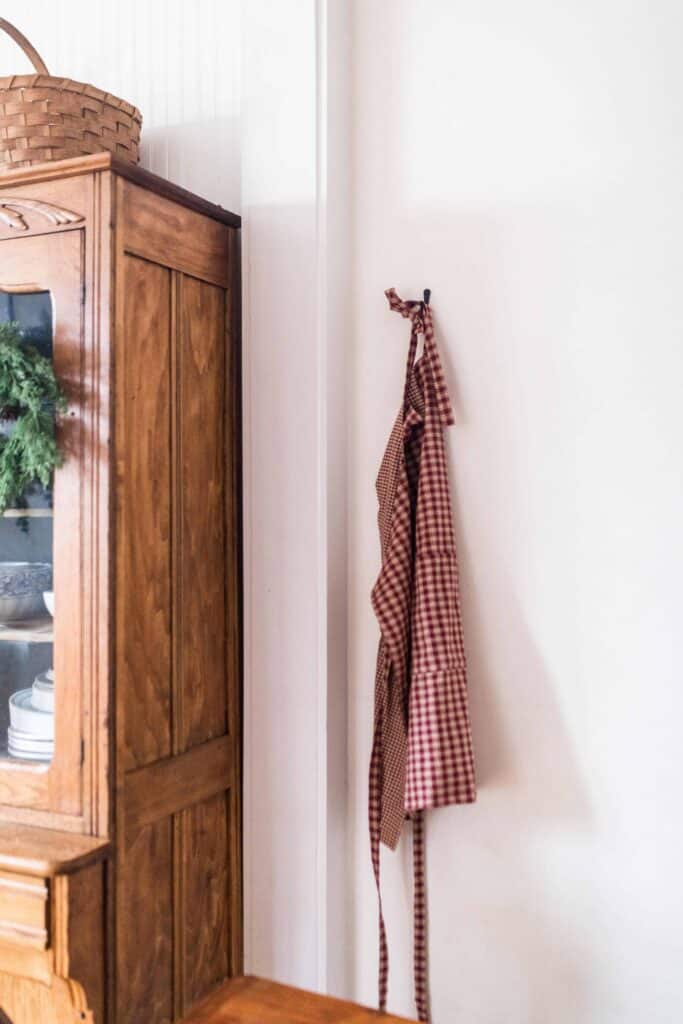 diy reversible apron on a hook next to a wooden china cabinet with a wreath