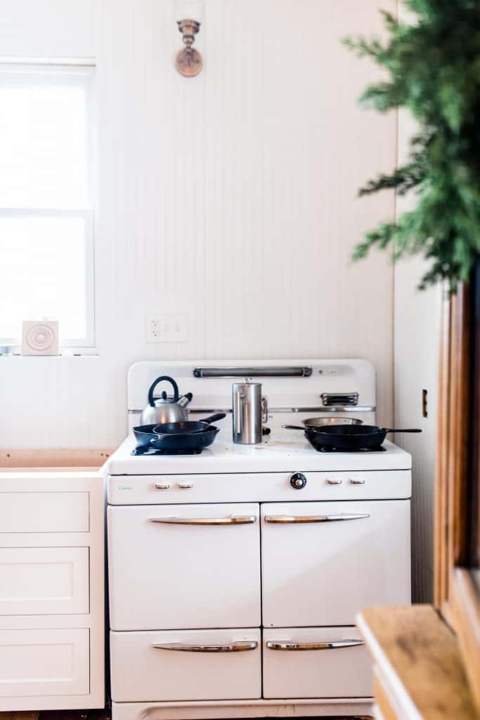 white antique stove with cast iron skillets on it. A white base cabinet without a countertop to the left.