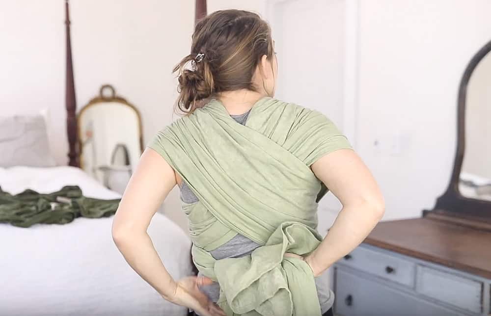 women tying woven wrap tails behind her back to create a secure wrap