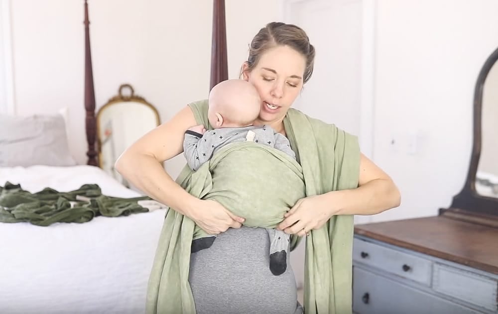 women putting baby in a green woven wrap tucking the wrap under the baby's butt to create a deep seat