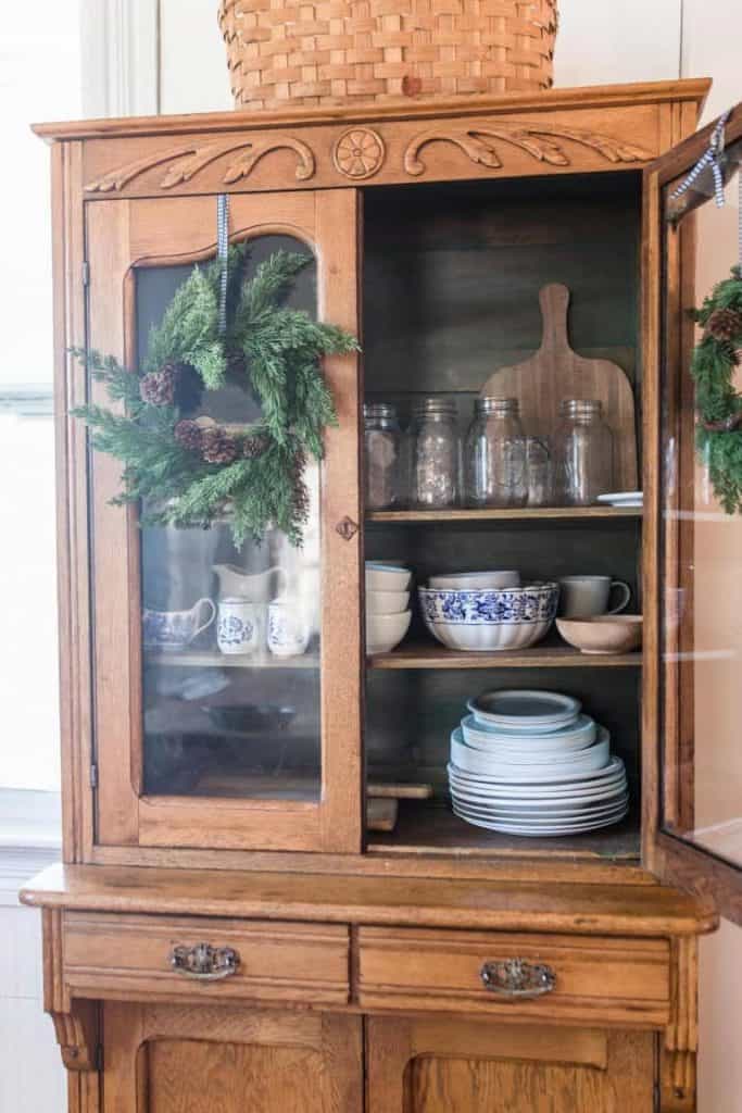 large wood China hutch with the door open showing dishes and mason jar glasses