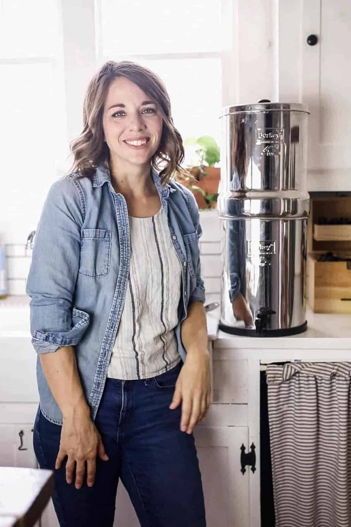 A woman standing next to a boroux water filter in a kitchen.