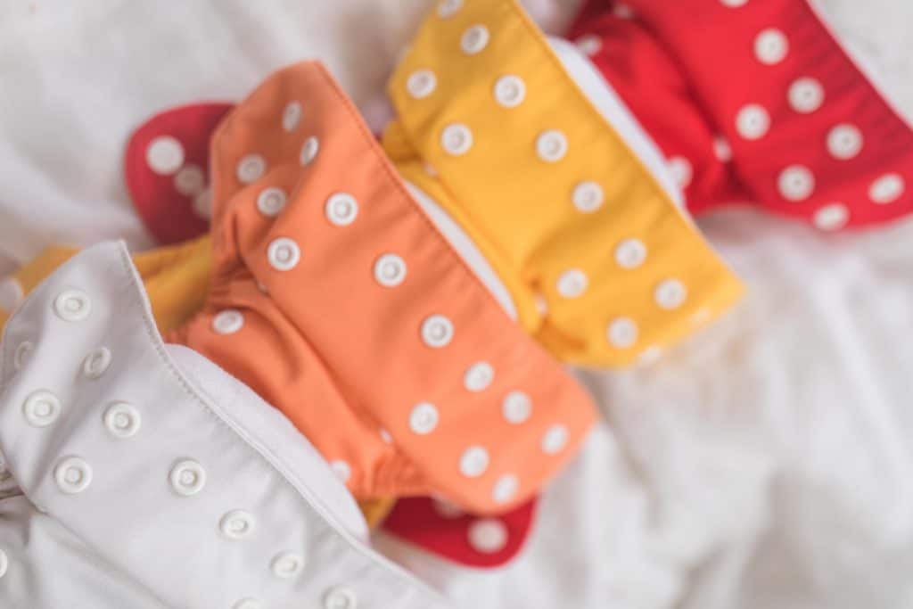 four newborn cloth diapers lined up in white, orange, yellow, and red