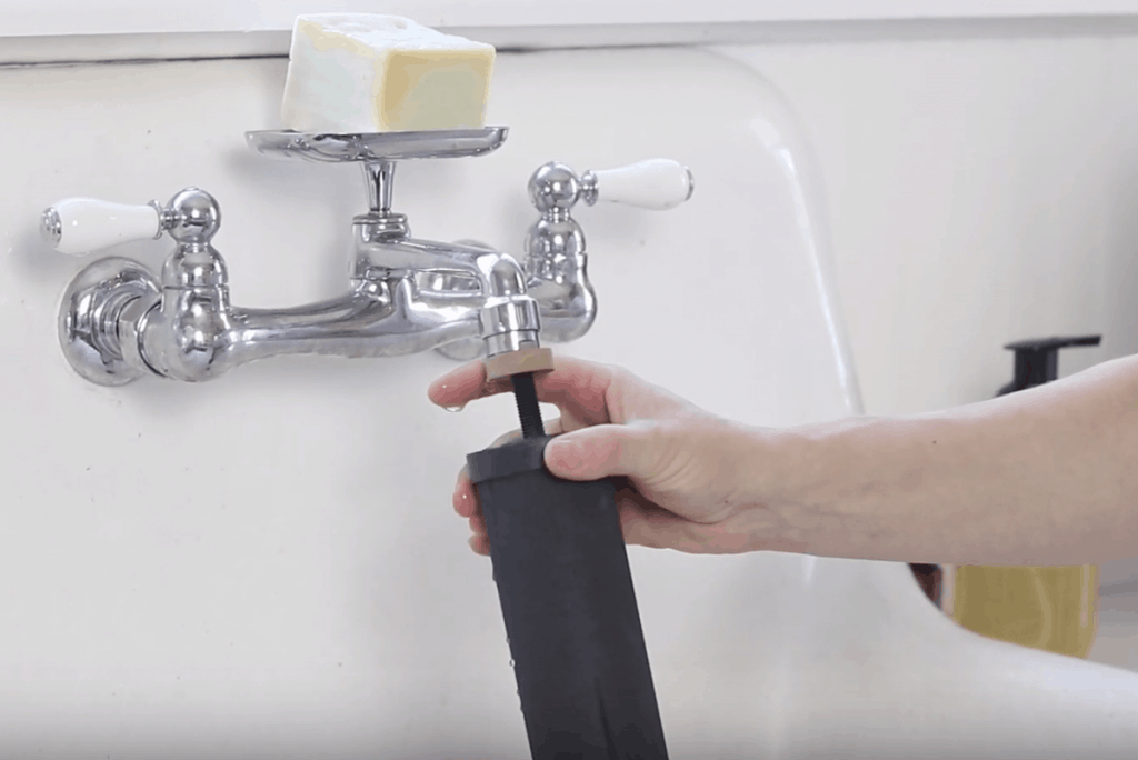 hand placing Black Berkey filter element onto running faucet to prime the filters