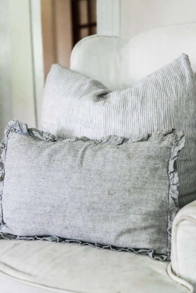 gray DIY ruffle pillow cover on a chair with a large pillow behind it.