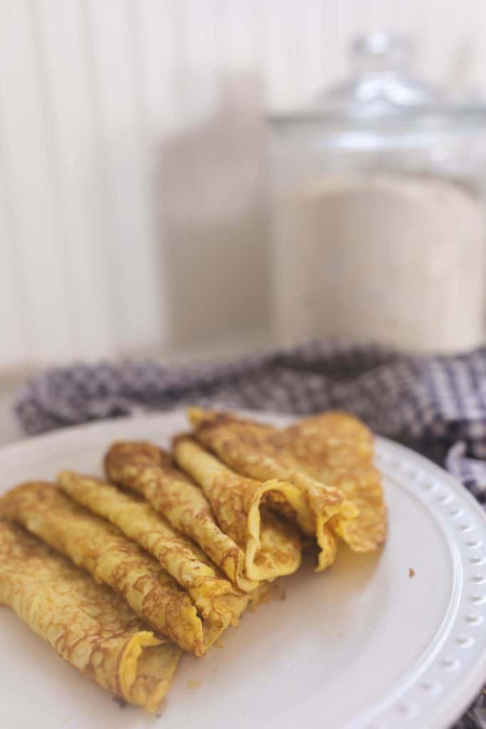 sourdough crepes rolled up on a white plate with a blue towel in the background