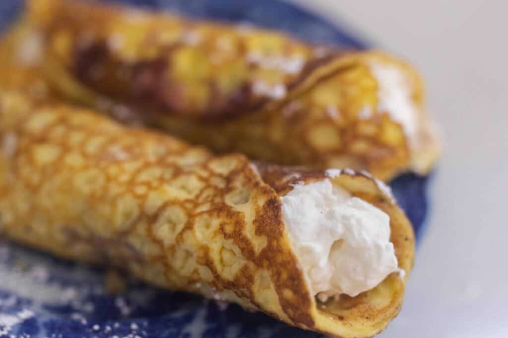 sourdough crepes rolled up with whipped cream cheese filling on a blue plate