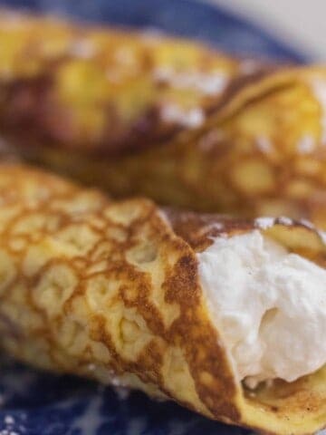 sourdough crepes rolled up with whipped cream cheese filling on a blue plate
