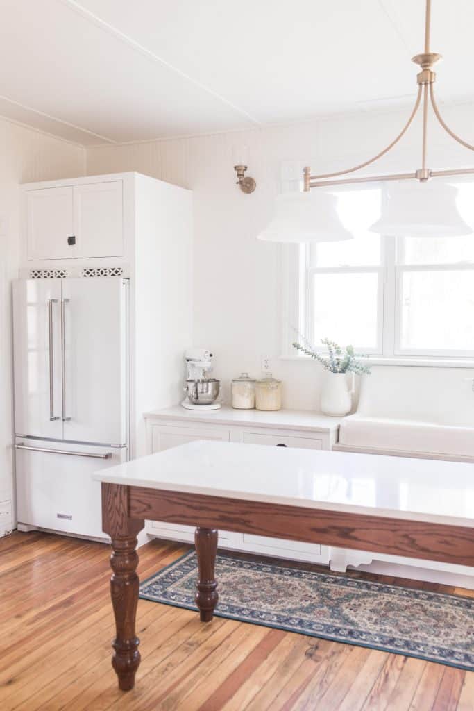 Victorian farmhouse kitchen with marble topped work table, with a white fridge with cabinetry surrounding the fridge behind