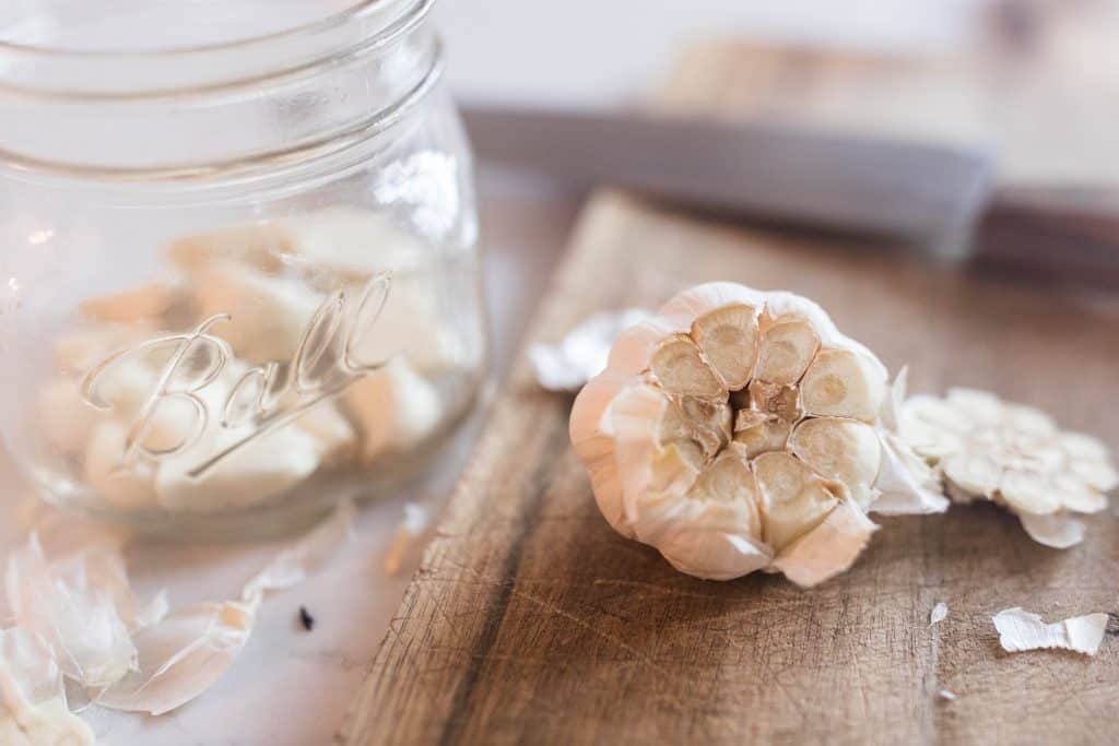 head of garlic with the top cut off with a jar of peeled garlic cloves in a jar to the left