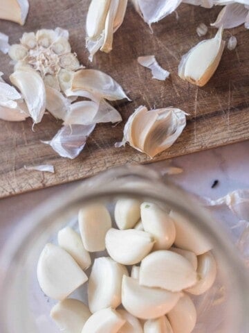 peeled whole garlic cloves in a jar with a cutting board with garlic peels above it