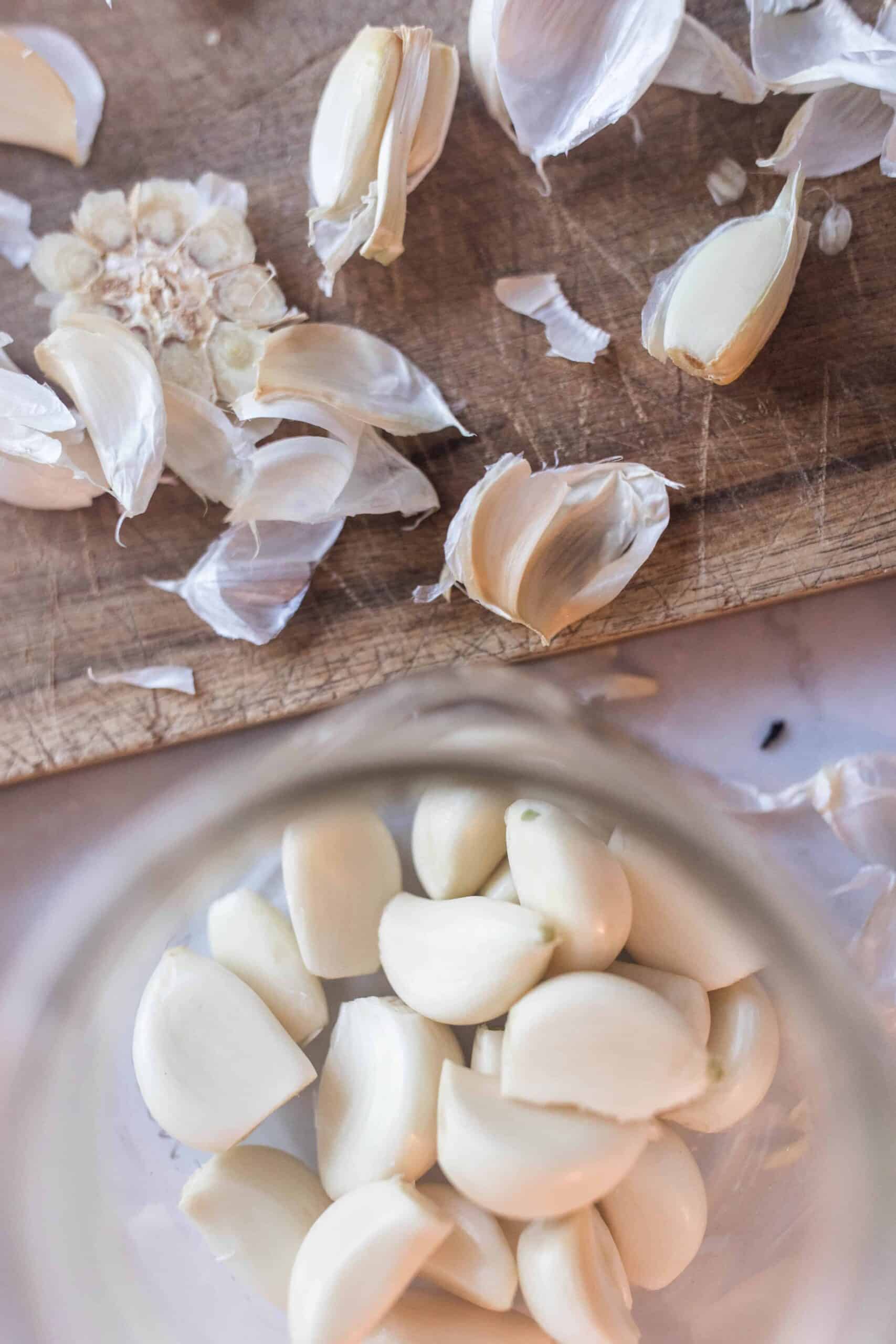 peeled whole garlic cloves in a jar with a cutting board with garlic peels above it