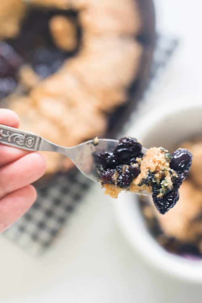 fork with a scoop of sourdough blueberry cobbler with more cobbler in the background