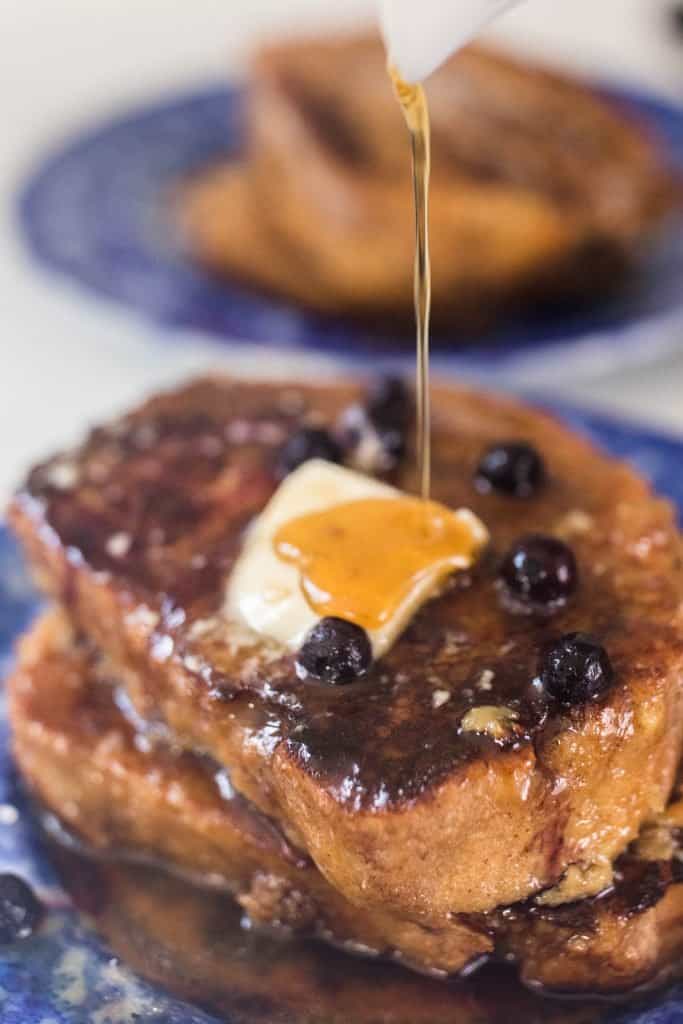 maple syrup being poured over sourdough French toast with blueberries