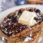 close up shot of two slices of sourdough French toast with butter and blue berries on a white plate