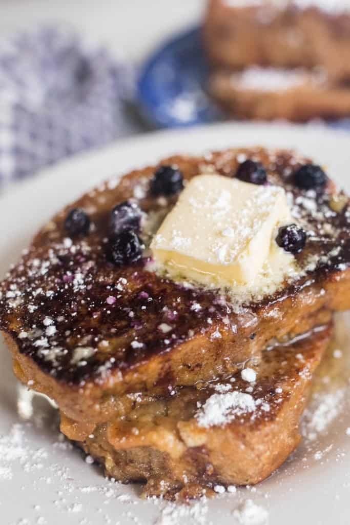 close up shot of two slices of sourdough French toast with butter and blue berries on a white plate