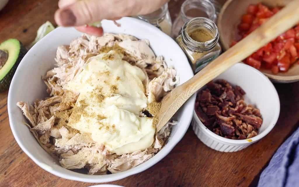 shredded chicken, mayo, and seasonings in a bowl. A hand is squeezing fresh lime juice over the chicken.