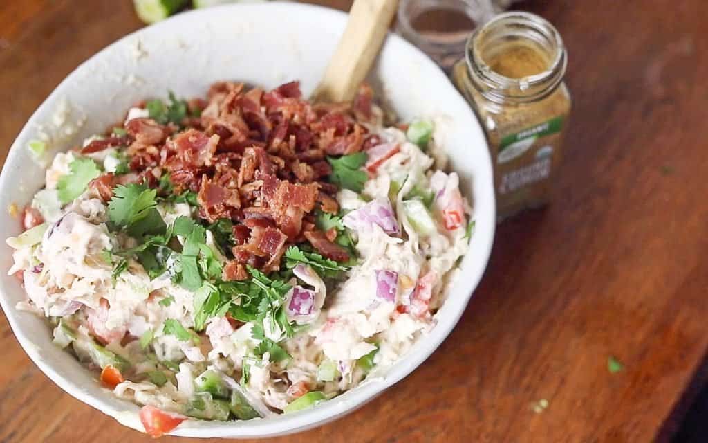 bacon and cilantro added to a bowl of chicken salad