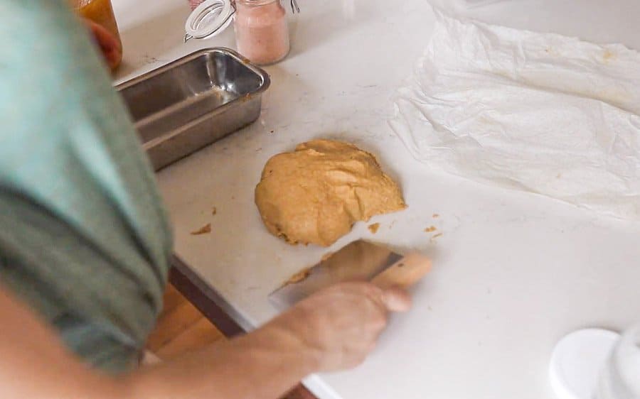 women using a dough scraper to form a ball of dough for bread